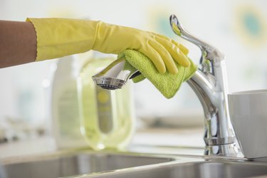 Womans hands in rubber gloves polishing kitchen faucet.