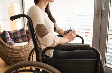 Unrecognizable young disabled woman in wheelchair at home.