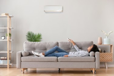 African female lying on couch use airconditioner breathing fresh air