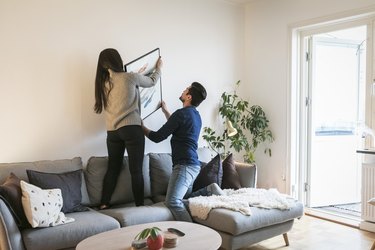 Couple adjusting painting on wall while leaning on sofa at home