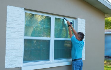 Homeowner caulking window weatherproofing home against rain and storms