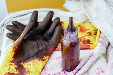 Bottle of hair dye and stained rubber gloves on a bathroom counter.