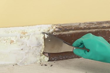 Using a scraper to remove paint from skirting board covered with paste stripping solution