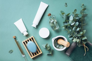 White cosmetic bottles, eucalyptus flowers, towels, soap on green background. Top view, flat lay. Natural organic beauty product concept. Spa, skin care, body treatment