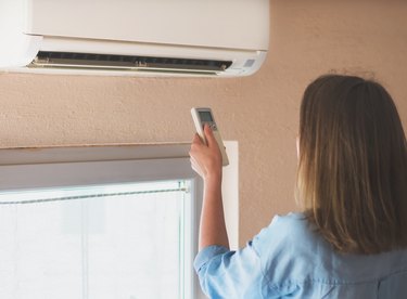 Woman holding remote control aimed at the air conditioner.