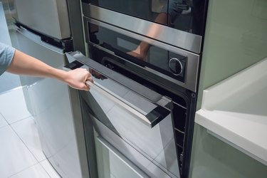 Woman's Hands open the black and silver door of oven machine for cooking