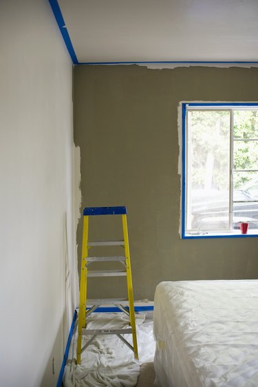 Ladder by bed covered with plastic in a half painted room