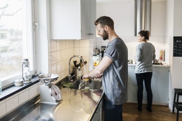 Man washing pan while woman standing in background in kitchen