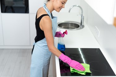 Young adult woman cleaning electric stove in kitchen