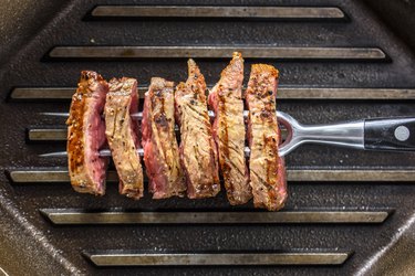 Slice of Grilled Steak with Seasoning  on a Fork and Cast Iron Grill