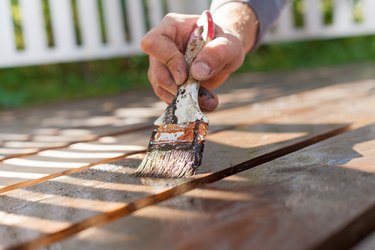 Hand holding a brush applying varnish paint on wooden surface