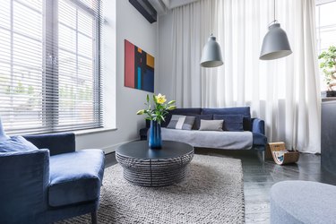Gray living room with blue upholstered furniture, white mini blinds and curtains, gray pendant lamps.