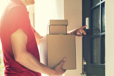 delivery service courier ringing the house doorbell with boxes in hands