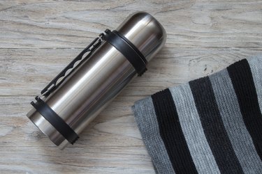 Thermos flask and scarf on a woden background. Top view