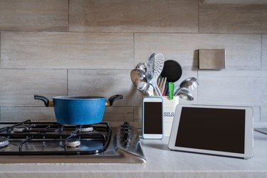 Kitchen top with stove, some utensils, a tablet and a mobile phone