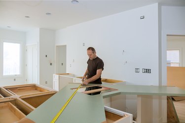 Man using tape measure for measuring size of wooden countertop in modern kitchen for home improvement.