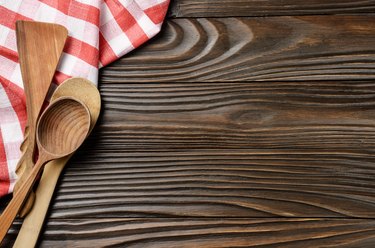 Red checkered napkin and wooden utencils on brown wooden kitchen table with copy-space. Top view