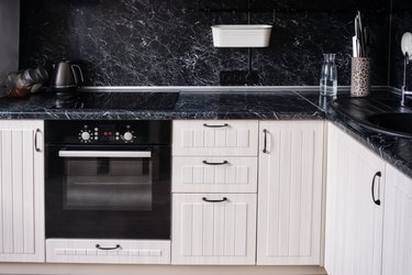 White wooden kitchen with black countertop and apron. Kettle, hob with oven