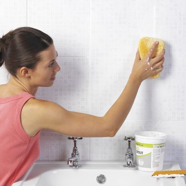 Woman cleaning tile wall in bathroom