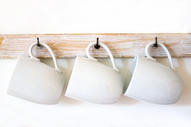 White Cups Hanging on Hooks, White Background, Copy Space