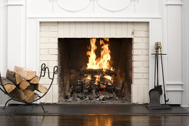 White brick wood-burning fireplace with split logs, fireplace tools, and fire burning.