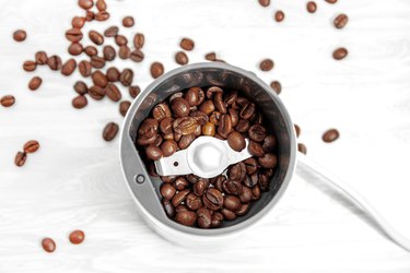 Top view on electro coffee grinder close-up with grains of coffee scattered around on a wooden table.