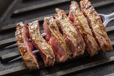 Slice of Grilled Steak with Seasoning  on a Fork and Cast Iron Grill