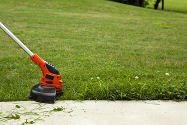 Using a string trimmer to cut longer grass and weeds at edge of pavement