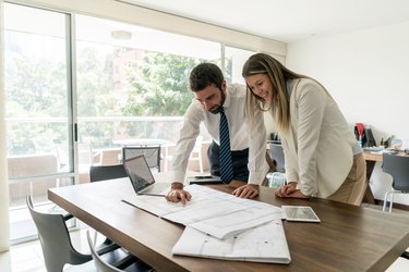 Happy team of architects discussing a project while looking at blueprints and laptop