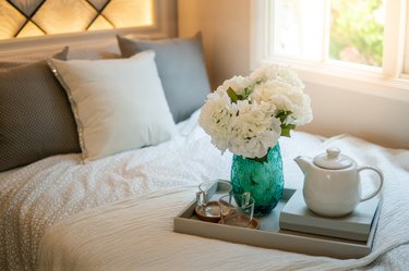 Bedroom decorative objects on the bed in cozy vintage bedroom. Flower vase, ceramic tea pot, glass cups and book. Home decoration concept