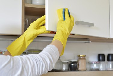 woman in yellow gloves washes the door in kitchen cabinet