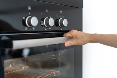 Woman holding handle modern built in oven and opening glass door