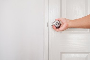 Hand of a person turning doorknob, white door and wall