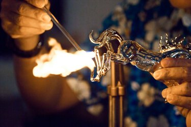 Glassblower heats the glass piece for shaping the future Christmas ornament