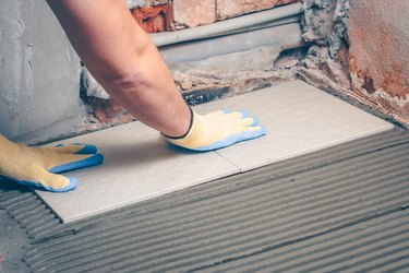 The tiler barks and fixes his hands in yellow gloves a square tile on the floor