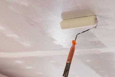 Workers are using paint roller on the ceiling