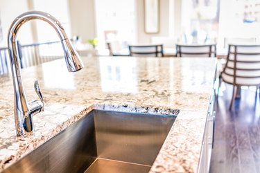 New modern faucet and kitchen sink closeup with island and granite countertops in model house, home, apartment.