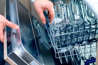 Man's hand opening dishwasher with clean utensils