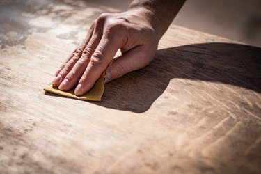 Gritty weathered man's hand sanding a wooden surface