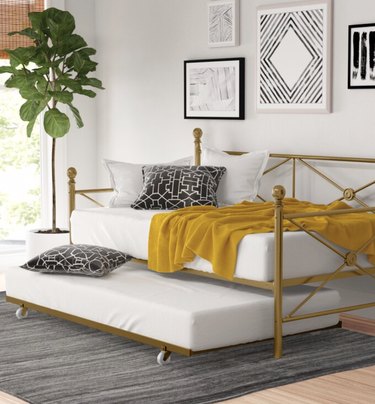 Small Space Daybed Ideas with Brass trundle bed with yellow blanket, pillows, plants, art, rug.