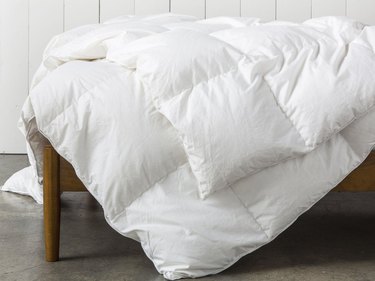 White down duvet on top of a wooden bed frame.