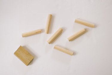 Six 5-inch wooden pegs next to sanding sponge