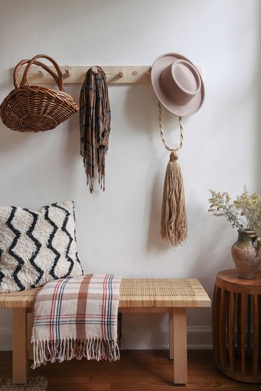DIY wooden peg rail hanging above bench with baskets, scarf and hat hanging from pegs