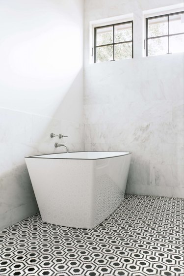 modern bathtub fixtures in marble bathroom with freestanding tub and two windows above it