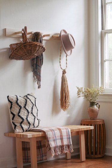 DIY wooden peg rail hanging above bench with baskets, scarf and hat hanging from pegs