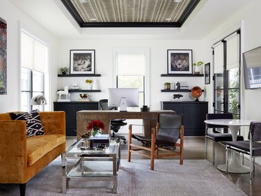 white modern home office with rust velvet sofa, wooden desk and black storage cabinets