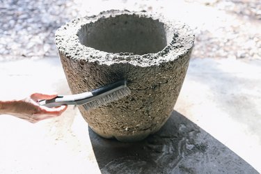 Scrubbing sides of hypertufa planter with wire brush to rough up surface