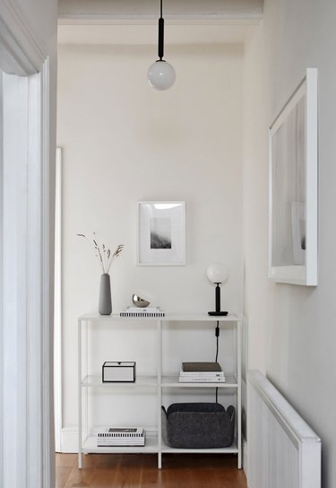 White hallway with globe pendant, globe table lamp, white shelves, art, vase.