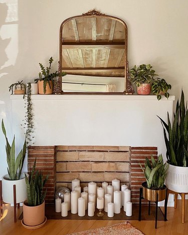 a fireplace surrounded by plants and decorated with simple white tall cylinder candles