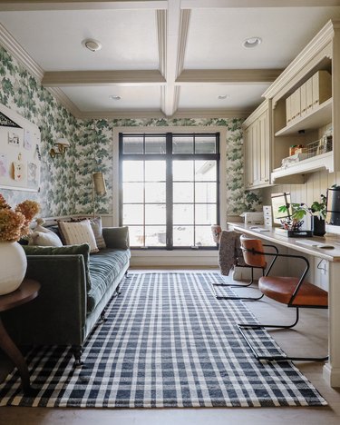 home office with leafy wall paper, built-in desk and large velvet sofa, gingham rug